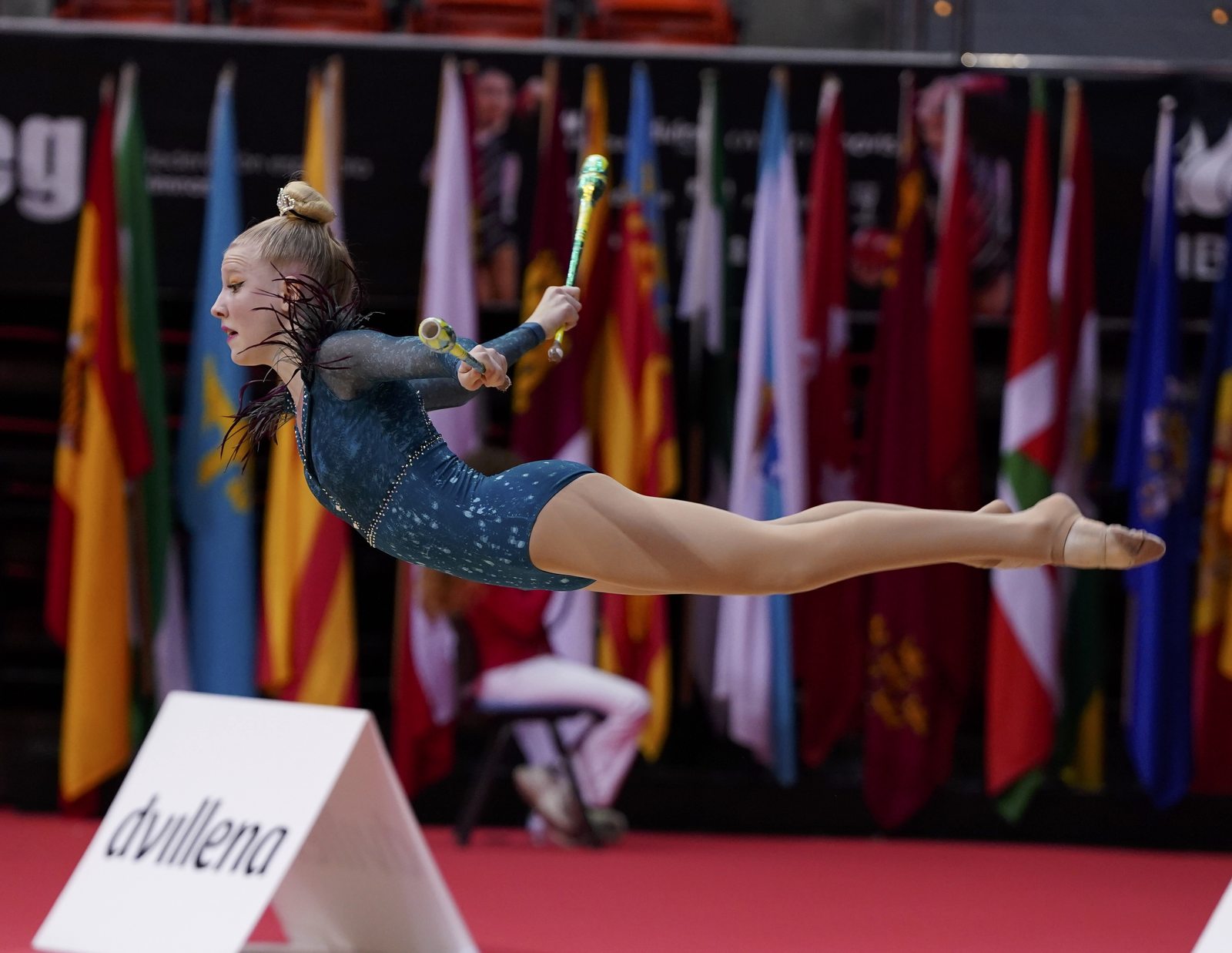 Gimnasta del club en un salto en spagat con las mazas durante una competición