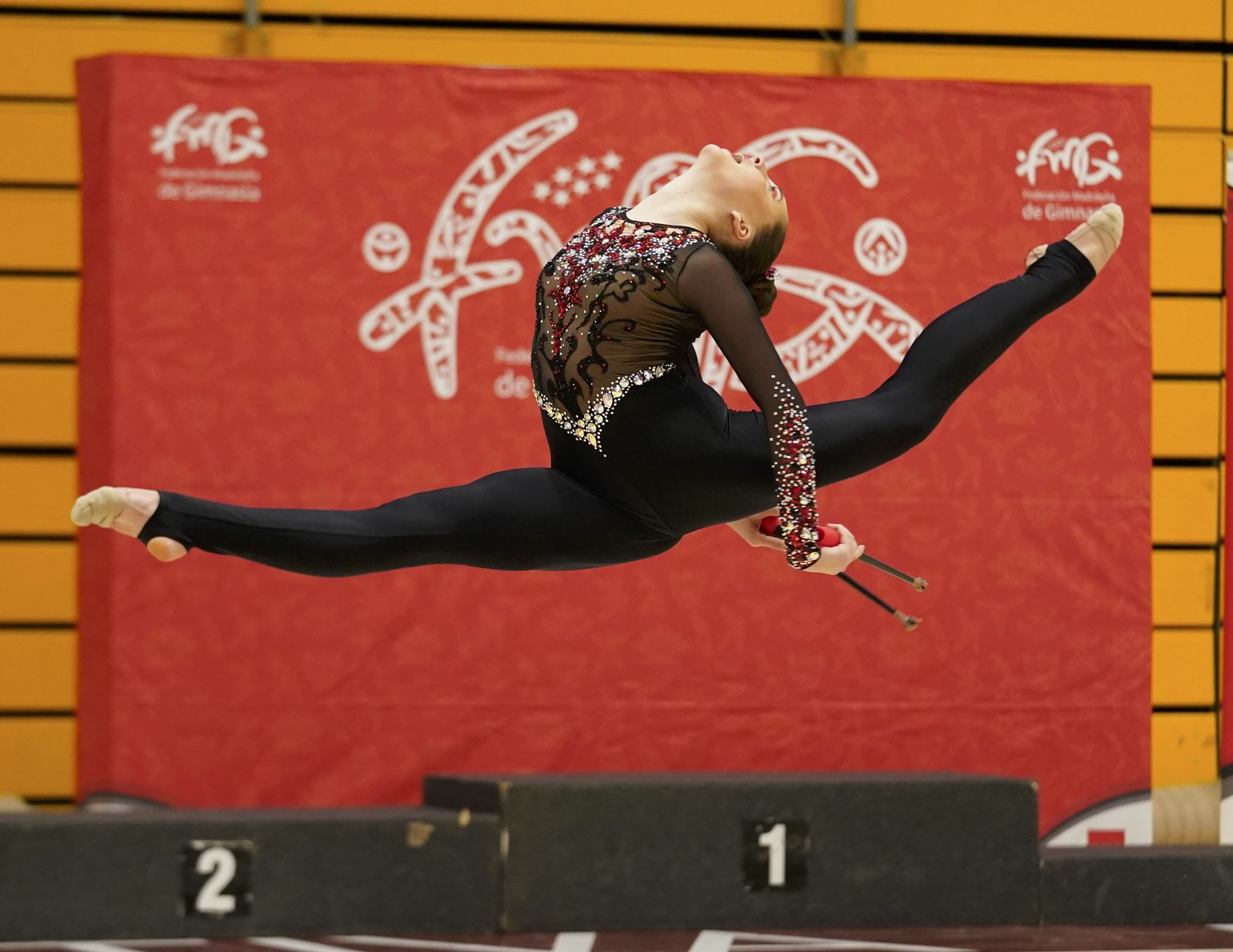 Gimnasta del club en un salto en spagat con las mazas